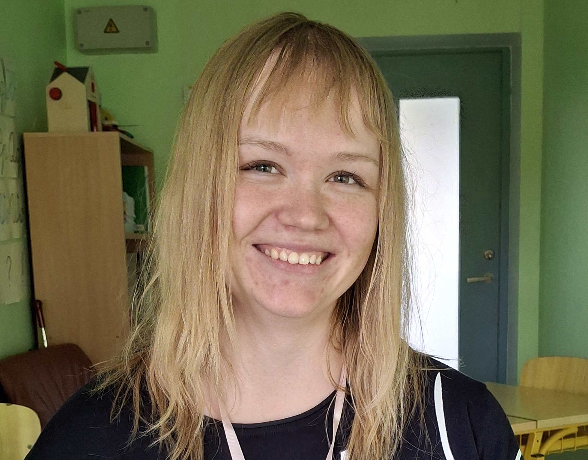 Naeratav heledapäine noor naine on roheliste seintega klassiruumis. 