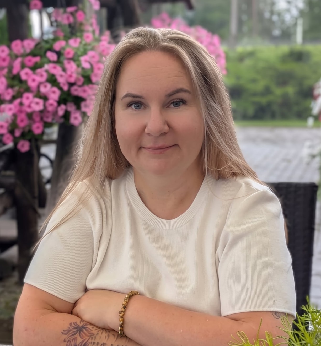 Pildil on heledate juuste ja valge särgiga naine, käed rinnal risti. 